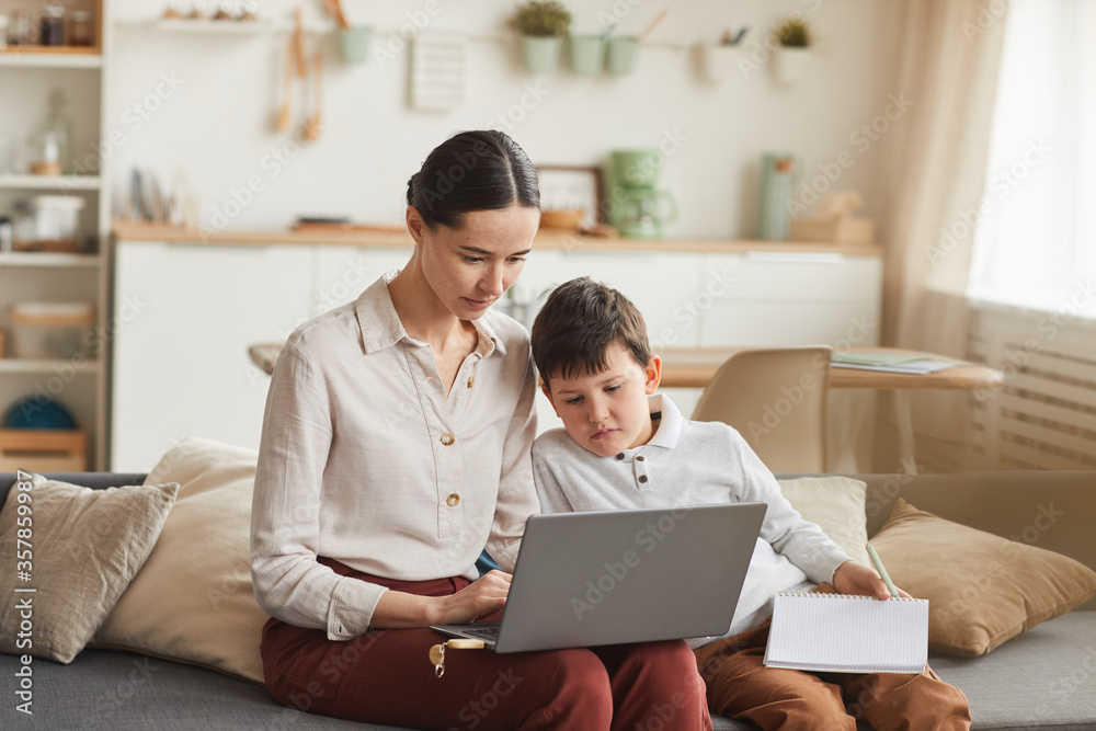 Warm-toned portrait of elegant young mother and son using laptop while studying at home in cozy interior, copy space Warm-toned portrait of elegant young mother and son using laptop while studying at home in cozy interior, copy space