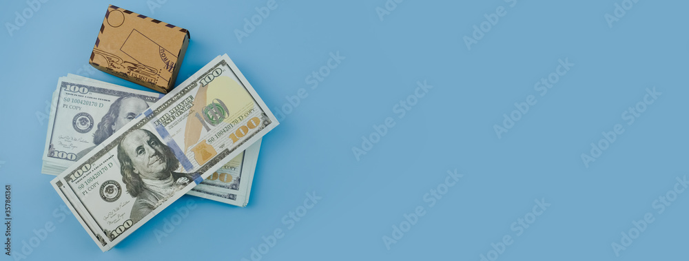 Top view of d banknotes US dollars and box or carton with copy space on blue background. -panoramic banner Top view of d banknotes US dollars and box or carton with copy space on blue background. -panoramic banner