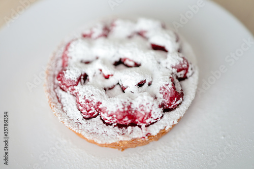 Raspberry tart covered with icing sugar on a white plate. 