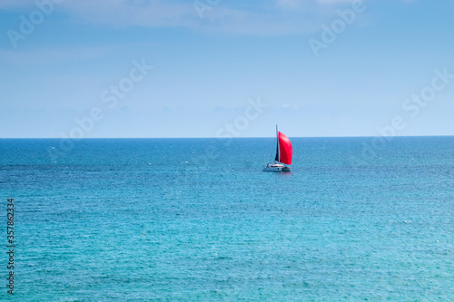Red ship on red sails. Blue sea and sky.