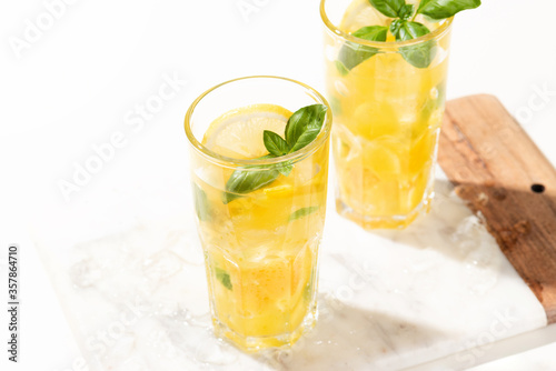 Citrus lemonade or mojito cocktail with lemon and orange and basil. Cold beverage or drink with ice on marble cutting board
