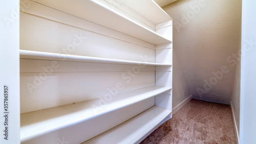 Panorama Small walk in closet with empty long cabinet shelves under slanted ceiling