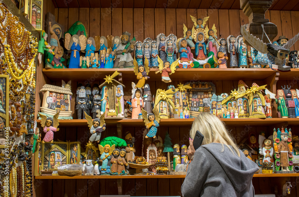Handmade souvenir shop in the Cloth Hall (Sukiennice) Krakow, Poland. Interior of little store in market with many Christmas wooden characters and amber jewelry. Woman-seller, who speak on the mobile