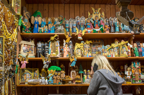 Handmade souvenir shop in the Cloth Hall (Sukiennice) Krakow, Poland. Interior of little store in market with many Christmas wooden characters and amber jewelry. Woman-seller, who speak on the mobile