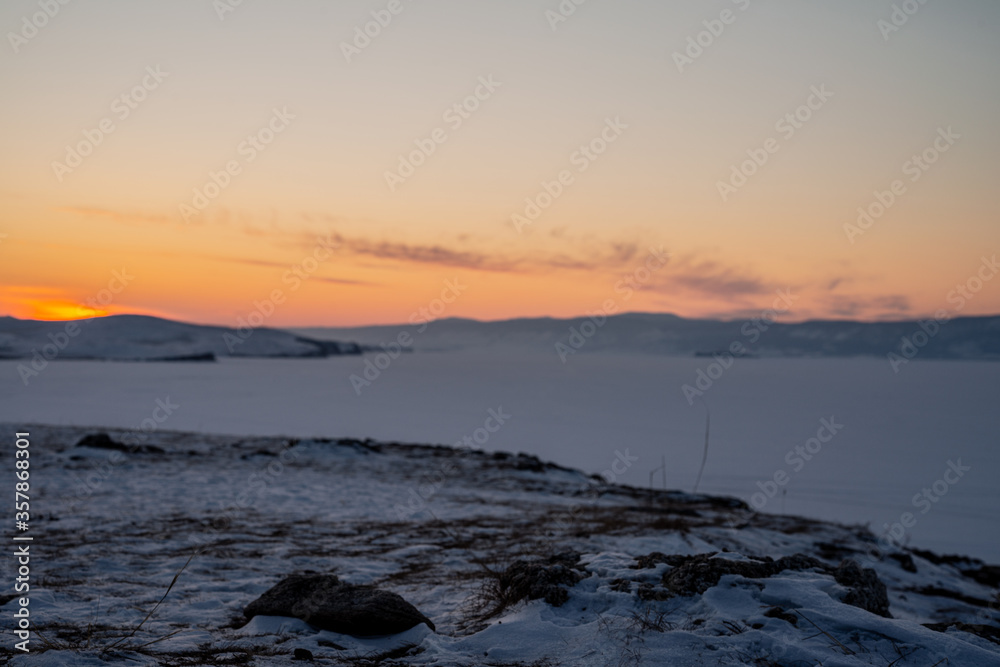 Shamanka rock on the sunset time with natural breaking ice in frozen water on Lake Baikal, Siberia, Russia.