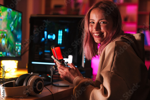 Image of girl using cellphone and smiling while playing video game