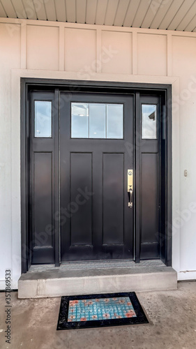 Vertical Black wooden front door with glass panes against panelled exterior wall of home