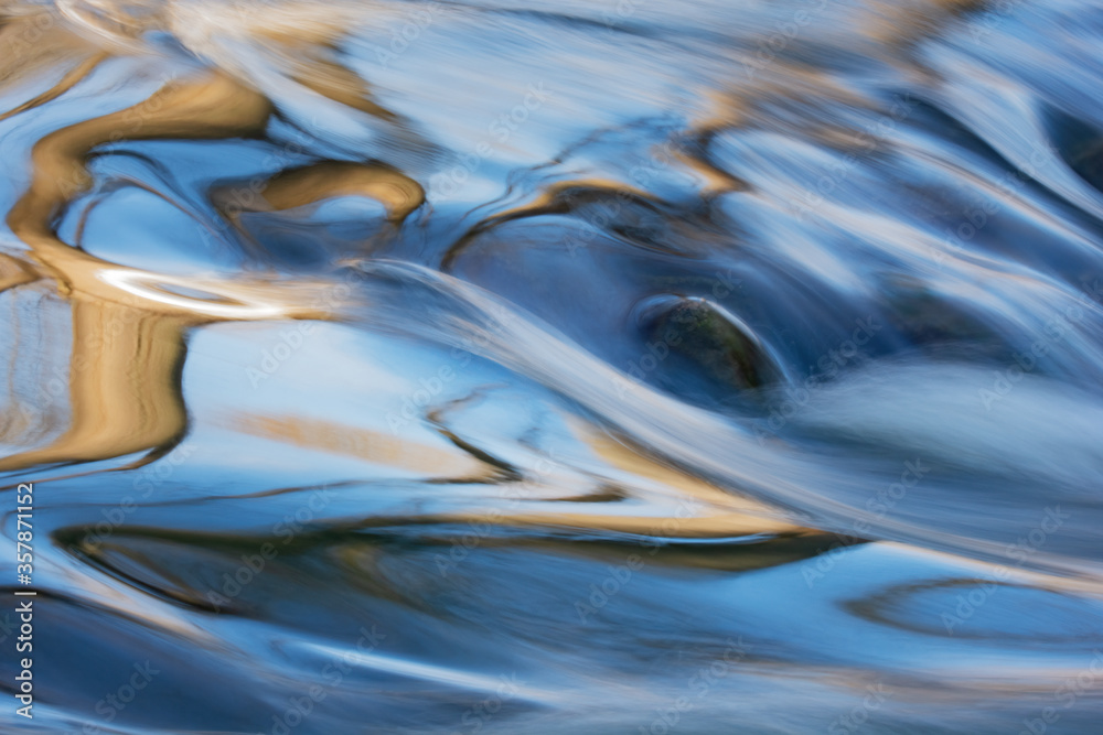 Summer landscape captured with motion blur of a rapids on the Rabbit River with abstract reflections of trees in calm water, Michigan, USA