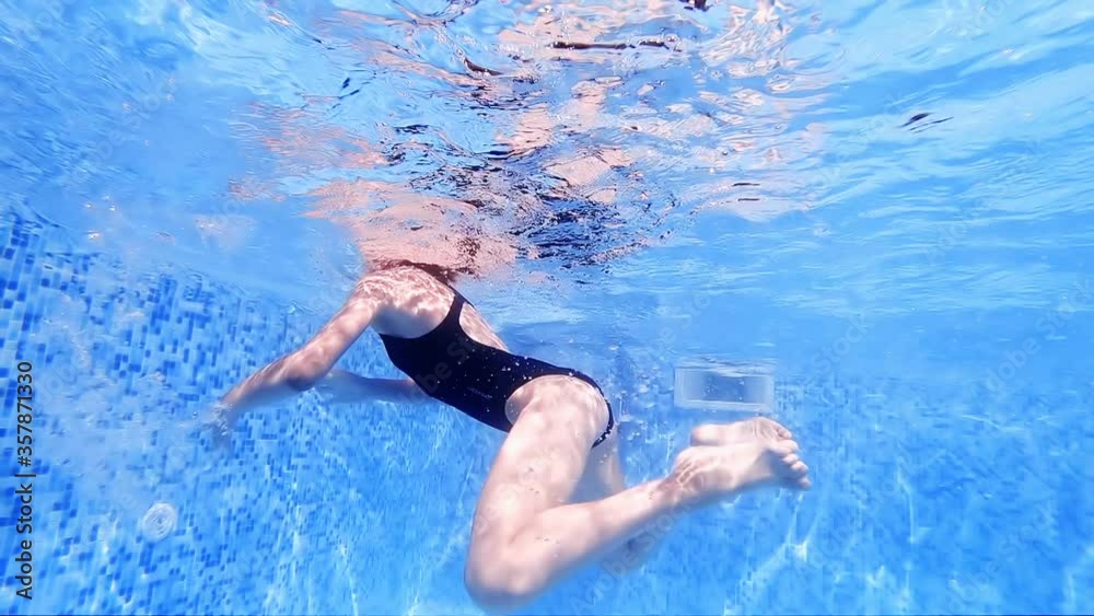Underwater view of female swimmer in swimming suit swimming in pool, slow motion