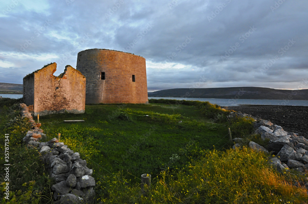 Ruines d'une tour et petite maison en pierre au bord de la mer, au coucher du soleil, en Irlande.