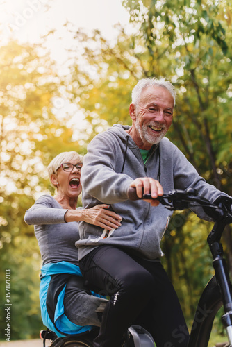 Active senior couple having fun in the park riding on the bicycle