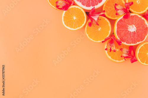 Composition made of slices of citrus fruits (orange, grapefruit) with red flowers in an orange background