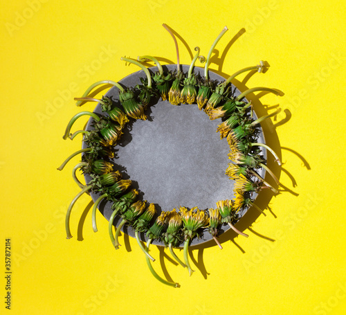 Top view of grey plate with dandelion flowers on bright yellow background