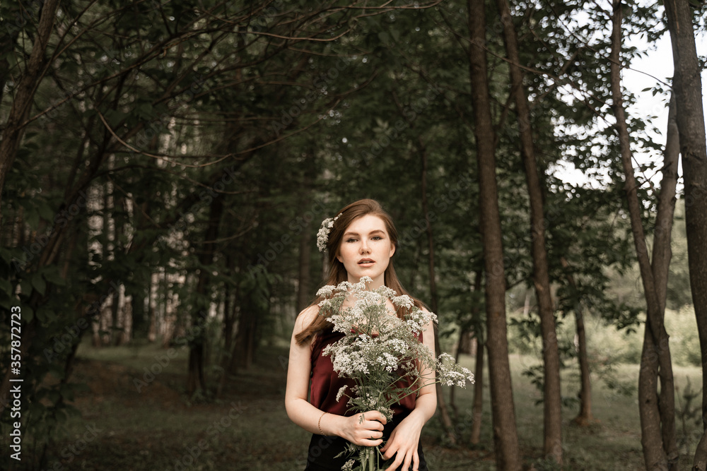 a red-haired girl with freckles on her face holds a forest bouquet in her hands, a girl with an unusual appearance stands next to the thicket