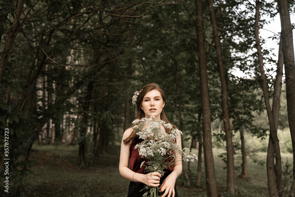 a red-haired girl with freckles on her face holds a forest bouquet in her hands, a girl with an unusual appearance stands next to the thicket a red-haired girl with freckles on her face holds a forest bouquet in her hands, a girl with an unusual appearance stands next to the thicket