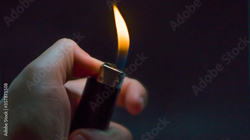 A person has lighters in his hands and he lights it through a flint wheel, the lighter ignites, sparks and fire appear, close-up on a black background. © Alina_Huzova