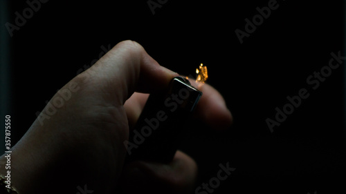 A person has lighters in his hands and he lights it through a flint wheel, the lighter ignites, sparks and fire appear, close-up on a black background.