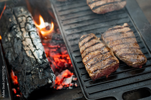 Beef steaks grilling on a cast iron plate on a camp fire. Campfire cooking. Outdoor BBQ. Selective focus.