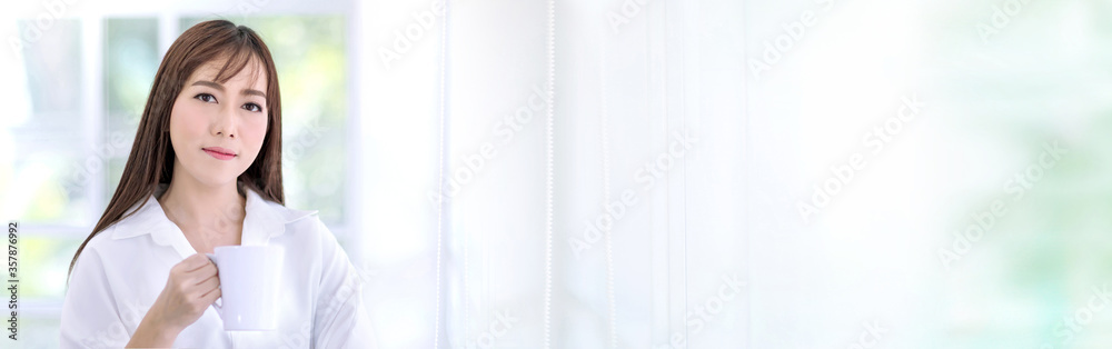 Beautiful Asian woman with long hair wearing a white shirt is holding a white cup and look at camera. Beautiful Asian woman with long hair wearing a white shirt is holding a white cup and look at camera.