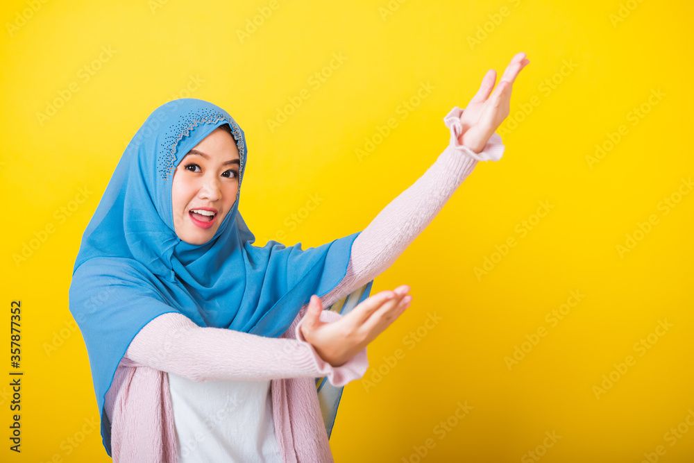 Asian Muslim Arab, Portrait of happy beautiful young woman Islam religious wear veil hijab funny smile she open arms for hug or raise hand to pick up items receive something from above isolated yellow Asian Muslim Arab, Portrait of happy beautiful young woman Islam religious wear veil hijab funny smile she open arms for hug or raise hand to pick up items receive something from above isolated yellow