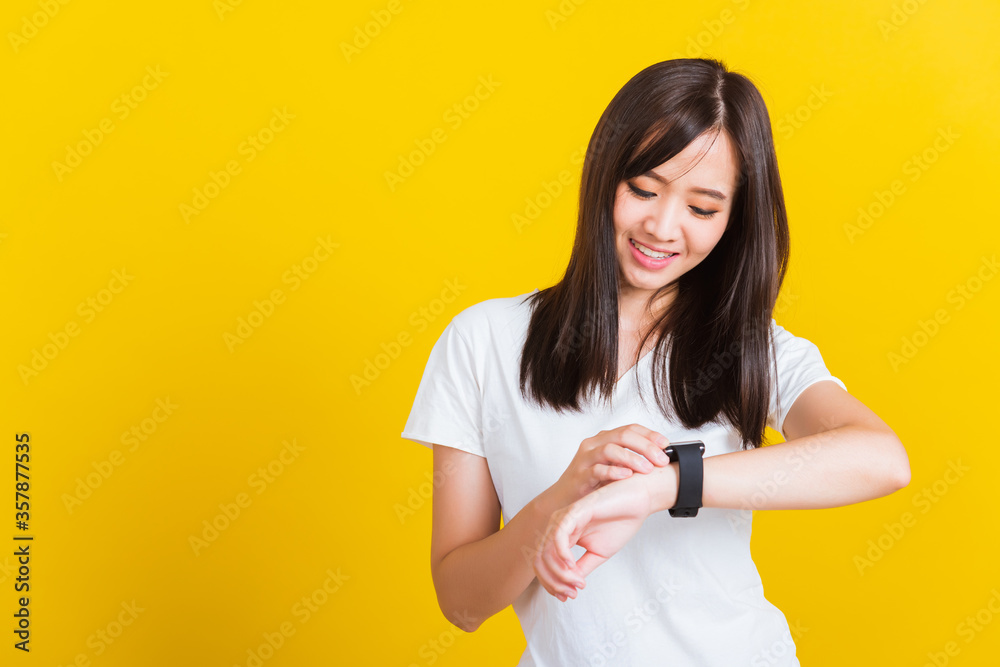 Portrait Asian of a happy beautiful young woman smiling looking and pointing finger her smart wristwatch studio shot isolated on yellow background Portrait Asian of a happy beautiful young woman smiling looking and pointing finger her smart wristwatch studio shot isolated on yellow background
