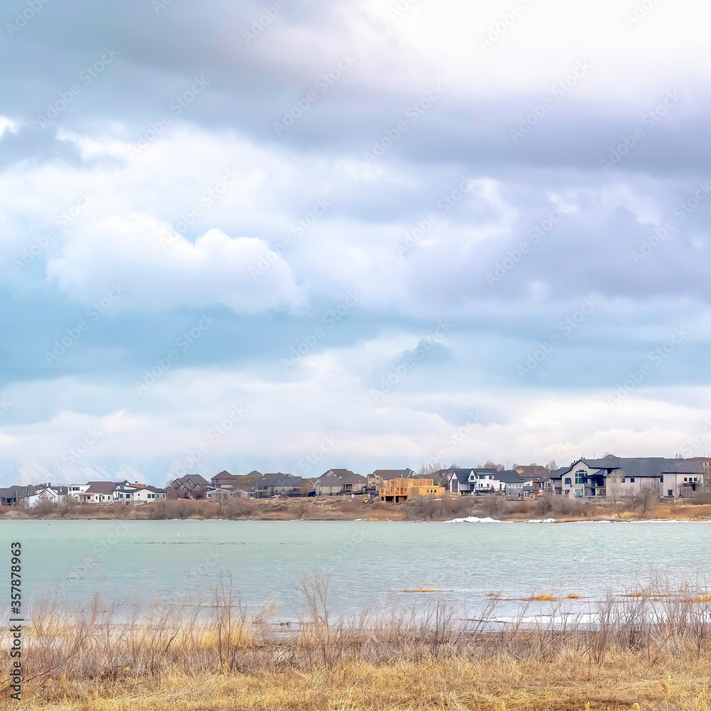 Square crop Scenic lake landscape with residences by the shore beneath sky with puffy clouds
