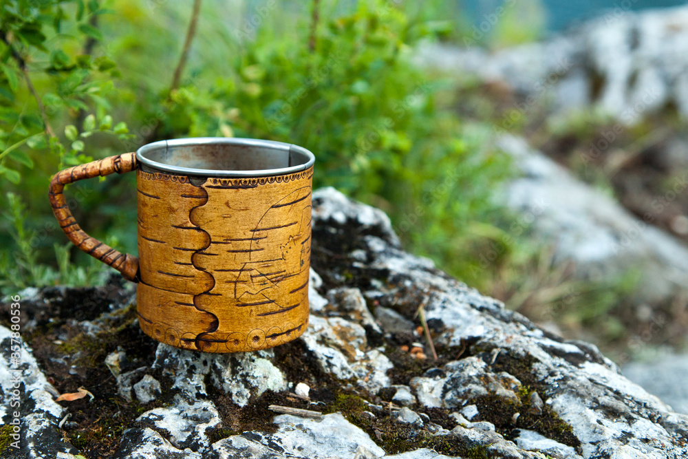 Obraz premium A steel mug with birch bark trim stands on the rocks.