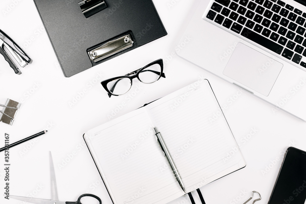 Top view white office desk table. Flat lay workspace with eye glasses, laptop, smartphone, clipboard, notebook and a pen, paper clip, pencil, offi supplies on white background Top view white office desk table. Flat lay workspace with eye glasses, laptop, smartphone, clipboard, notebook and a pen, paper clip, pencil, offi supplies on white background