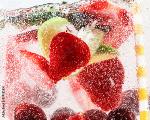 Close up view of cold and fresh lemonade with strawberry, cherry, mint leaves and ice cubes. Texture of cooling summer's drink with macro bubbles on glass. Fizzing or floating up to top of surface.