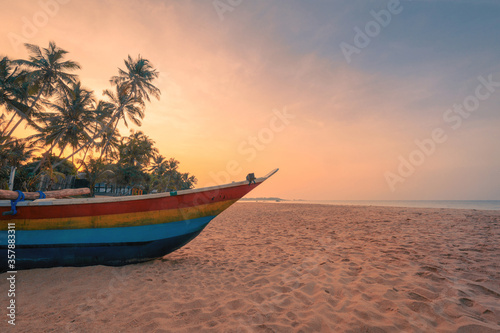 Traditional fisherman's wooden boat on the sand of Sri Lanka island beach on a ocean coast in front of village under coconut palm trees.