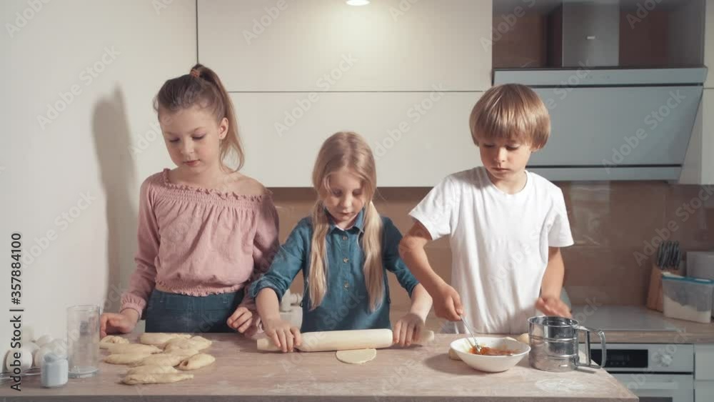 Children blond cook in the kitchen. Roll out the dough with a rolling pin. Children blond cook in the kitchen. Roll out the dough with a rolling pin.