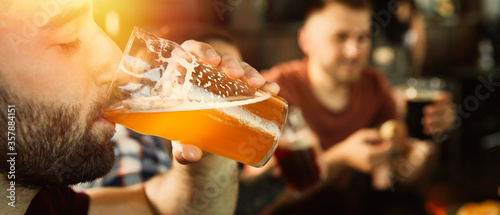 Young man drinking tasty beer in pub, space for text. Banner design