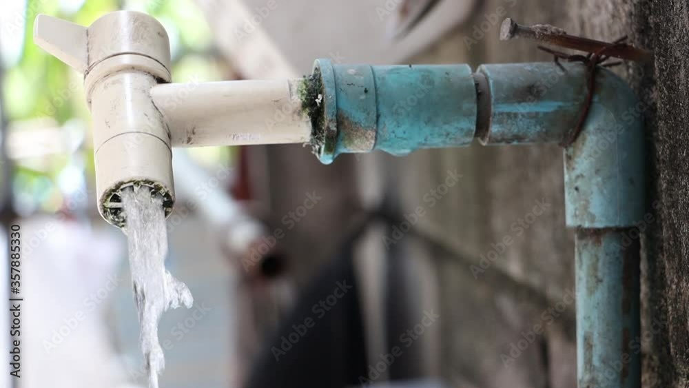 Water stream flowing from a faucet on plastic pipe, close up view. Water pouring from a tap from bricks wall on backyard, slow motion.