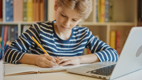 Smart Little Boy Uses Laptop for Learning, Writes Down Useful Information. Distance Learning, e-Education, e-Learning, Homeschooling Concept. Portrait of a Boy Doing Homework