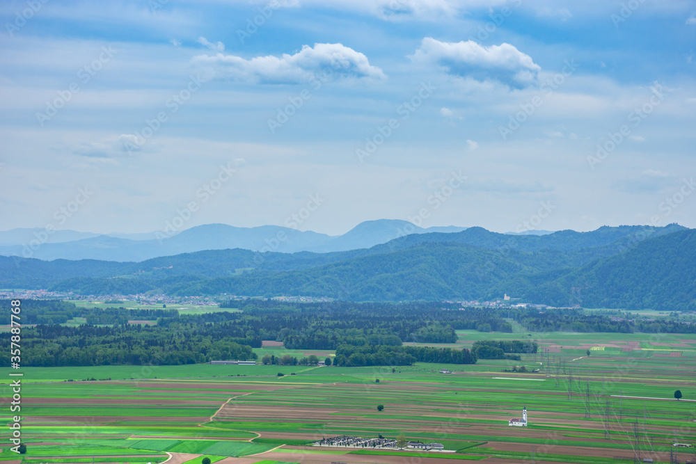 Fototapeta premium Slovenian countryside in spring with charming little church in the middle of a field and Julian Alps in the background