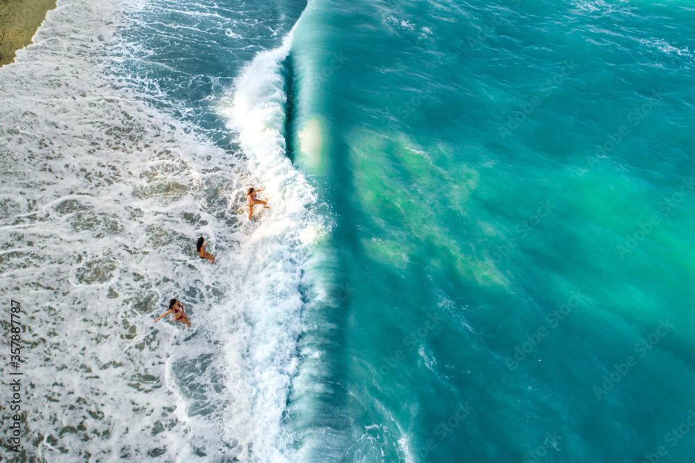 Fototapeta premium Drone view of group of children playing in the sea waves, kids getting hit by wave 