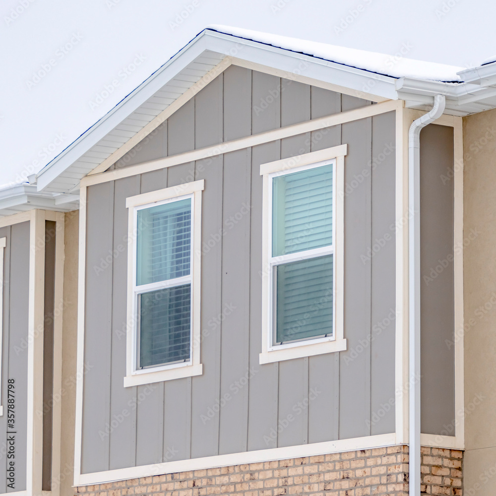 Square crop Snowy roof brick wall and vertical siding at exterior of townhome against sky Square crop Snowy roof brick wall and vertical siding at exterior of townhome against sky