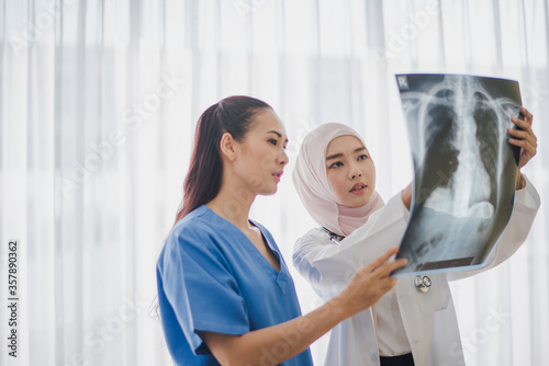 Young Asian woman Muslim doctor  giving advice discussion to patient standing near big window looking chest x-ray film at hospital which excite felling serious. Medicine and health care safe concept.