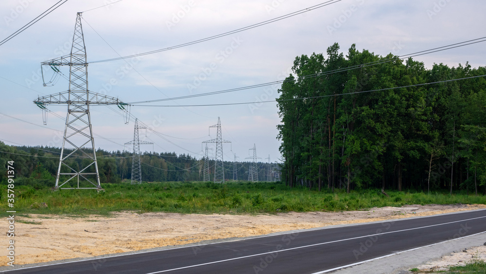Asphalt road on the background of electric poles with wires and woods.
