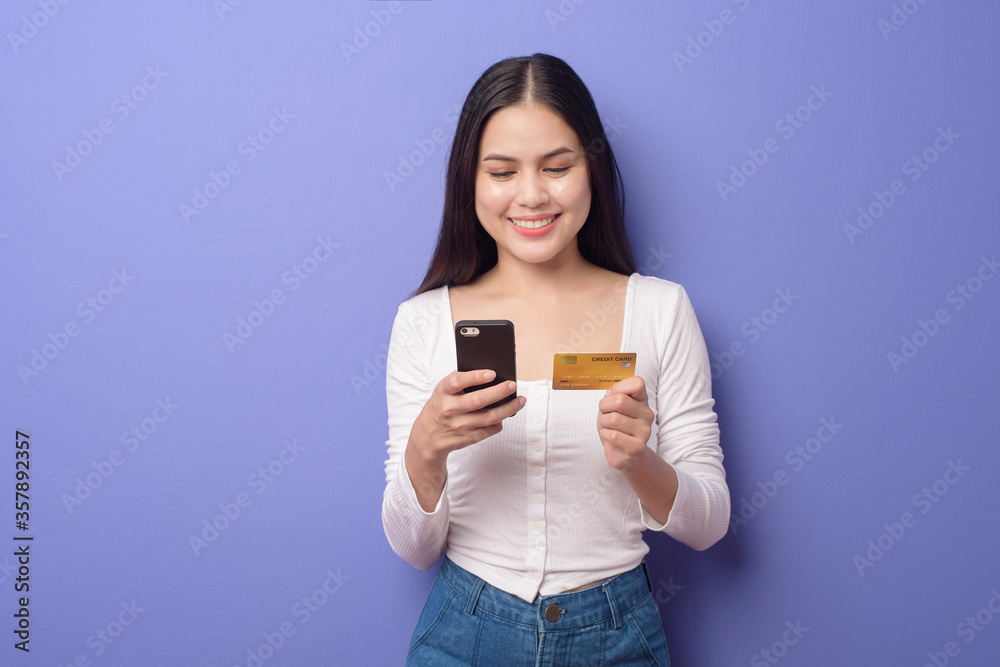 Portrait of Young Asian woman is using cell phone with credit card on purple background Portrait of Young Asian woman is using cell phone with credit card on purple background