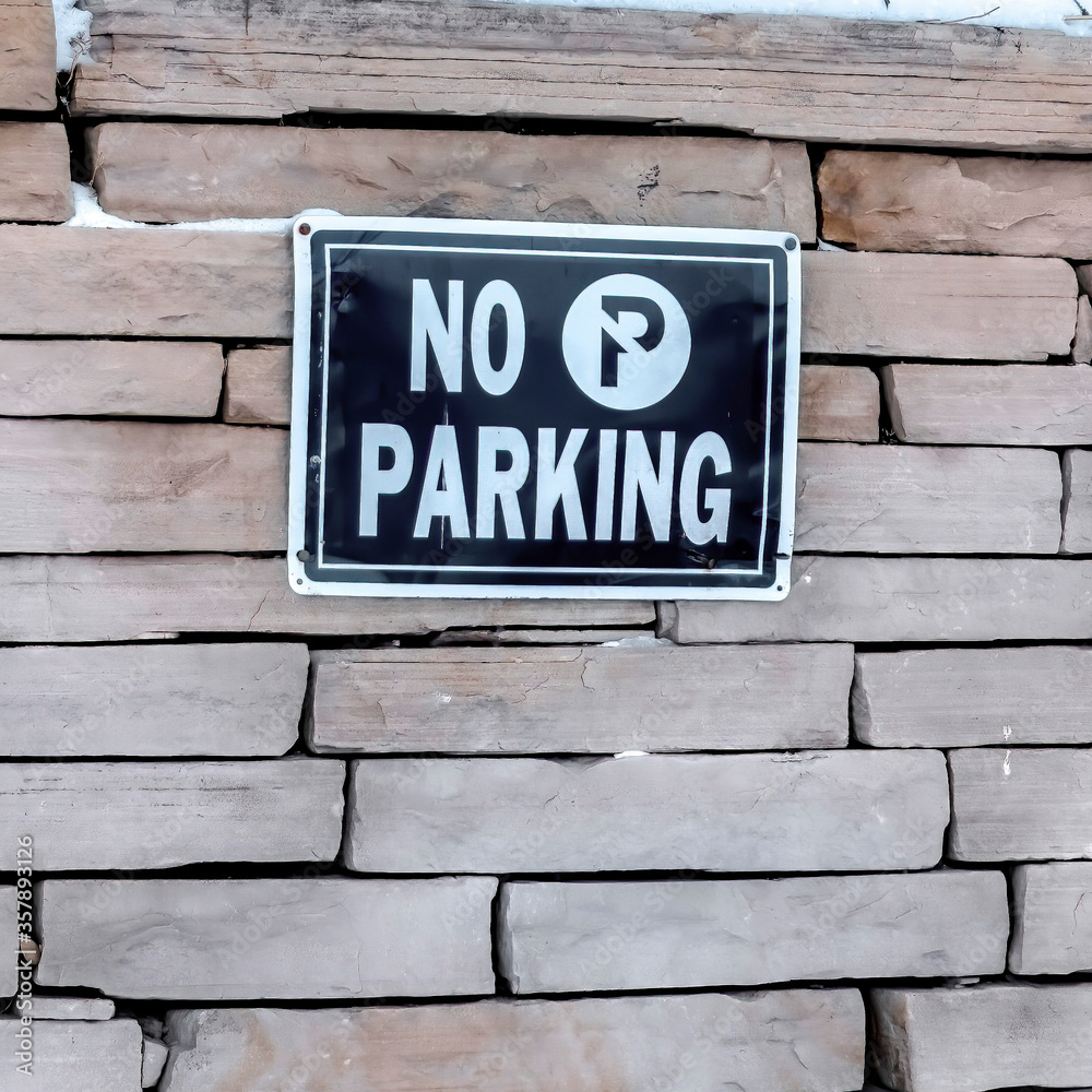 Square No Parking sign on a stone brick retaining wall topped with snow in winter Square No Parking sign on a stone brick retaining wall topped with snow in winter