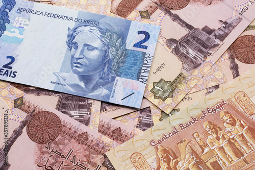 A blue two reais bank note from Brazil close up in macro with a background of brown Egyptian one pound bills