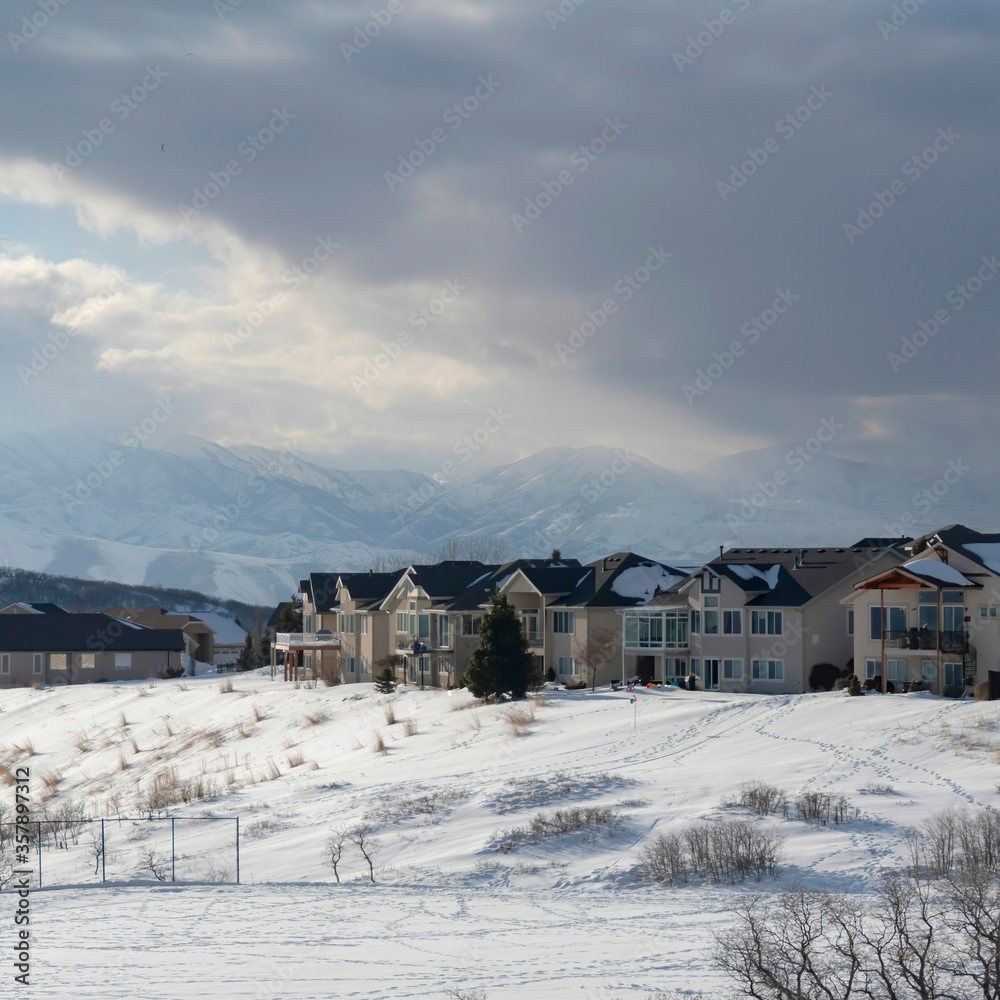 Square Homes on snowy terrain ovelooking Wasatch Mountain peak and dark overcast sky