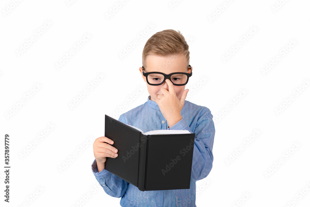 Cute dreamy schoolboy reads book and wearing glasses while standing in the studio, isolated over white Cute dreamy schoolboy reads book and wearing glasses while standing in the studio, isolated over white