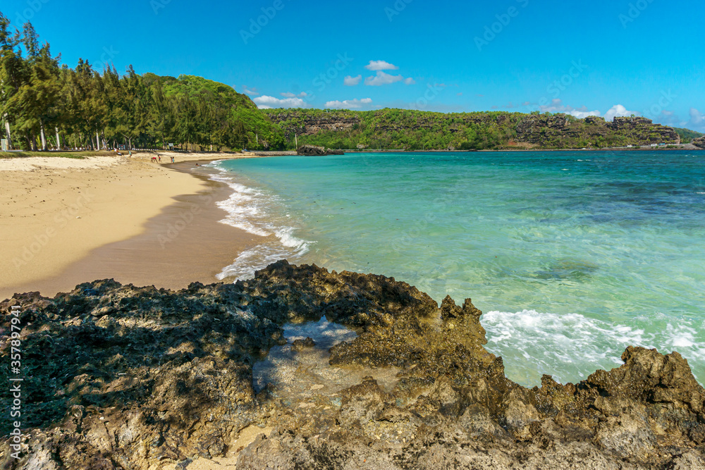 White sandy beach curving around small bay with black coral rocks in the foreground on Mauritius island