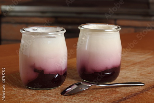 Yogurt with jam in open small glass jar with spoon on wooden cut