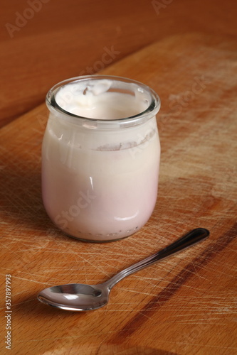Yogurt in open small glass jar with spoon on wooden cutting boar