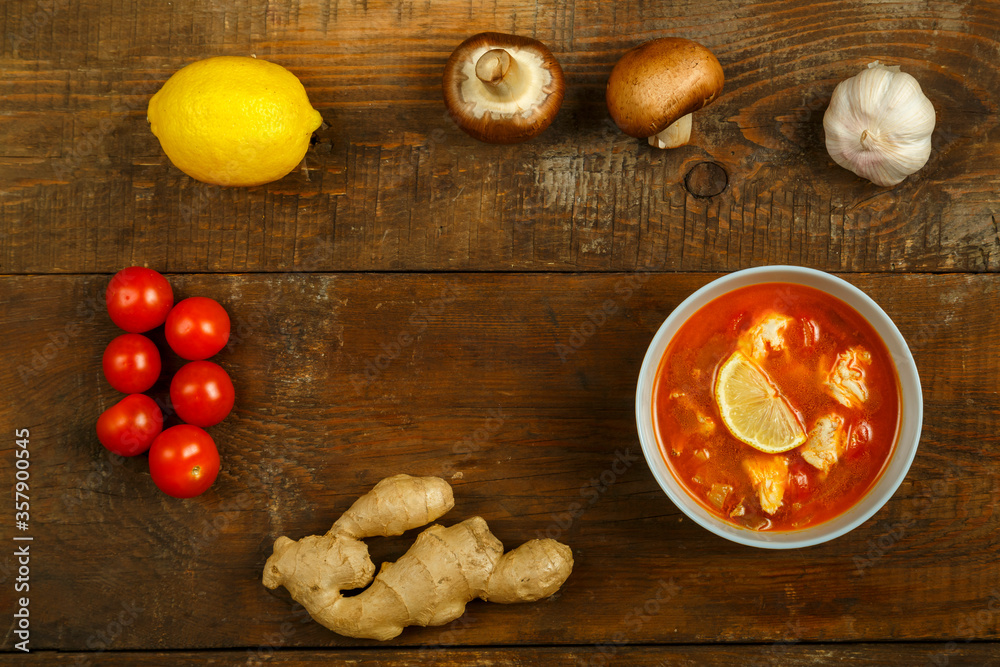 Fototapeta premium Traditional thai tom yam soup with chicken in a cup with spoon and vegetables nearby.
