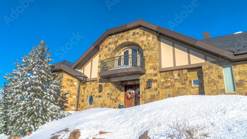 Panorama Stone home with small balcony over front door decorated with wreath in winter