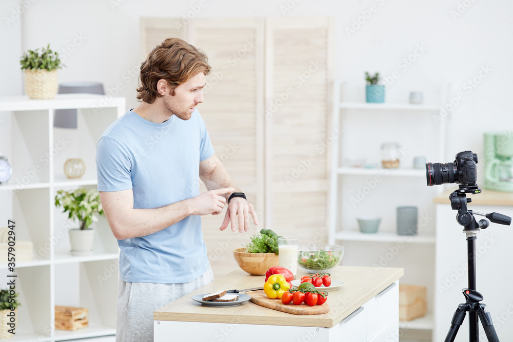 Young man pointing at his watch and telling about the time of healthy eating to the camera for his followers Young man pointing at his watch and telling about the time of healthy eating to the camera for his followers